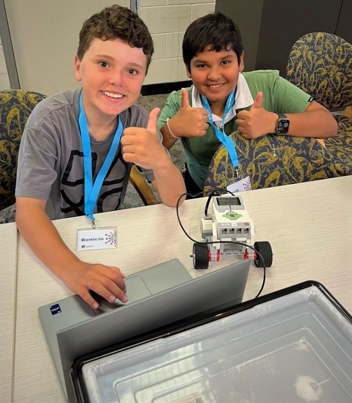 Two boys smiling at camera with their robot and computer