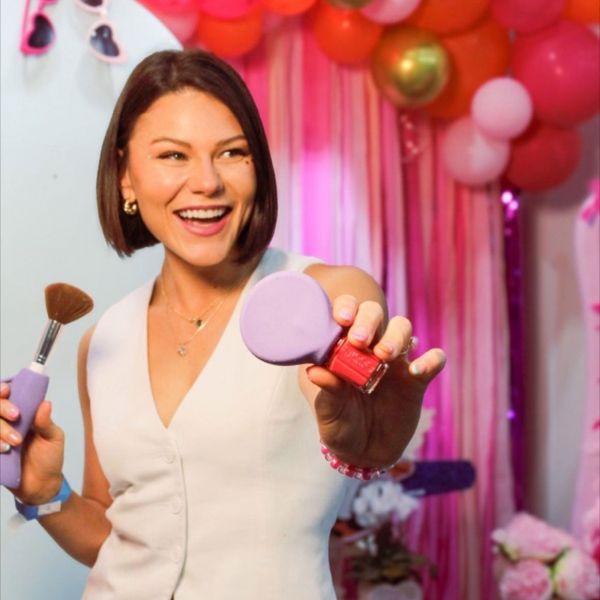 Storm is smiling while holding her accessible beauty products with a colorful balloon background.