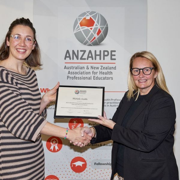 Two people shaking hands in front of a white background and exchanging a certificate.. Leader in Health Education Research