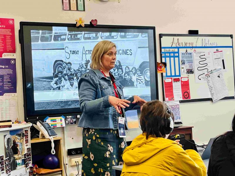 Head and shoulders shot of a middle-aged woman standing in front of a white board teaching a high school class