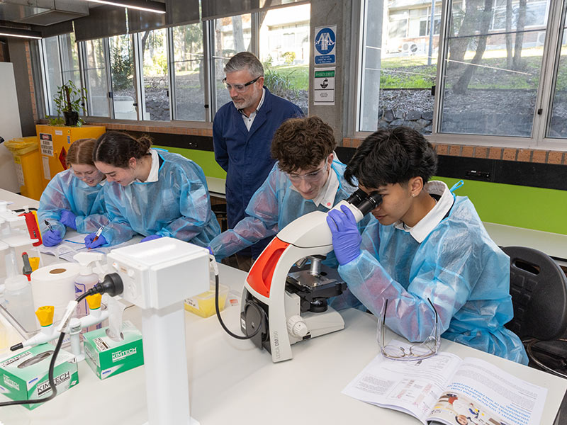 Students in lab gear look through microscopes