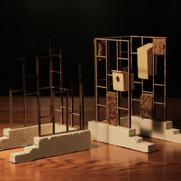 Miniature architectural models with metal frameworks and concrete bases on a wooden surface. The mood is warm and contemplative with soft lighting.