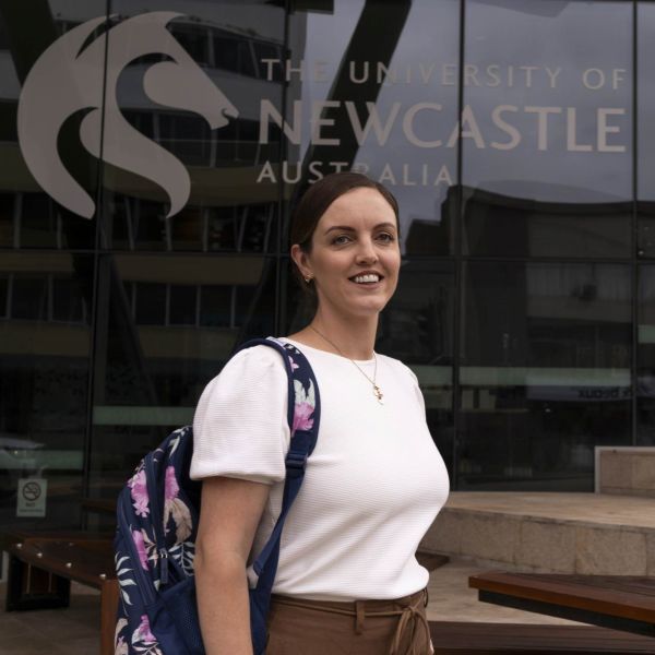Carly standing in front of building that has University of Newcastle branding.