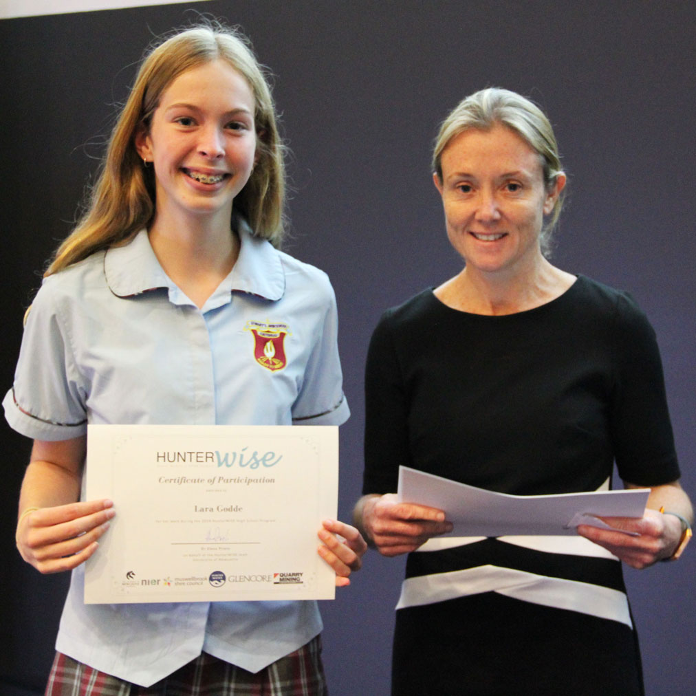 Lara stands holding her HunterWiSE participation certificate, standing next to a member of staff