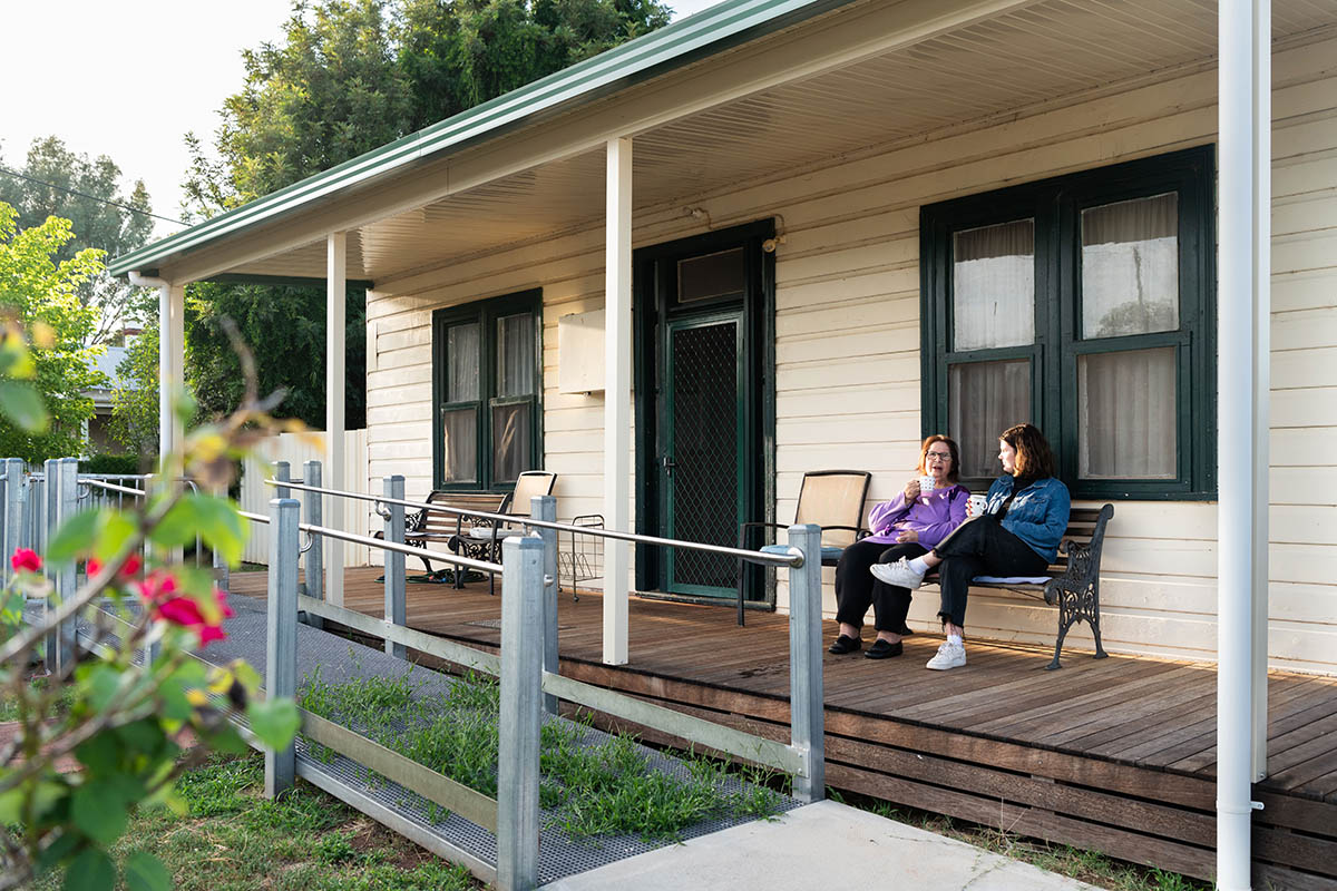 Two women sitting in front of a house