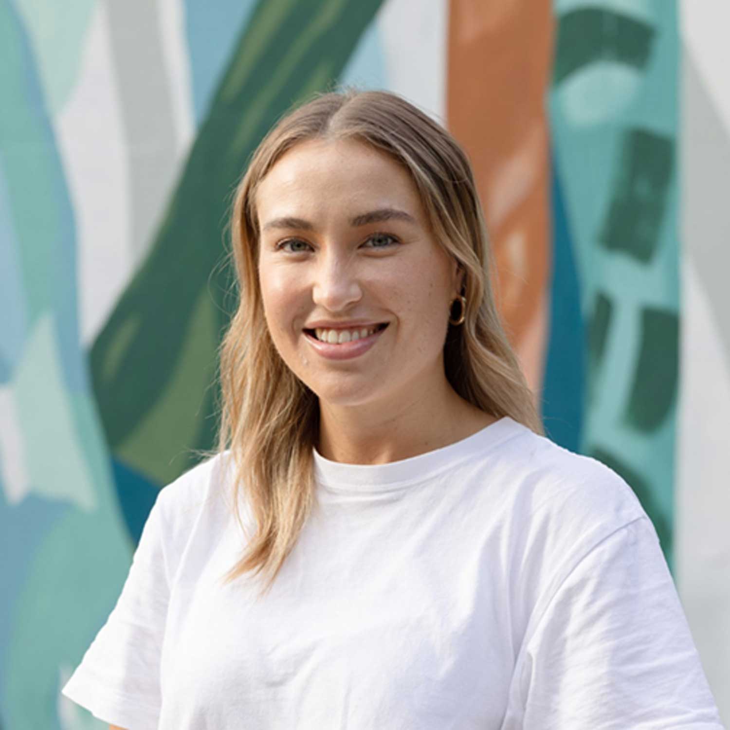 Blonde female smiling at the camera, pictured against a street art background.