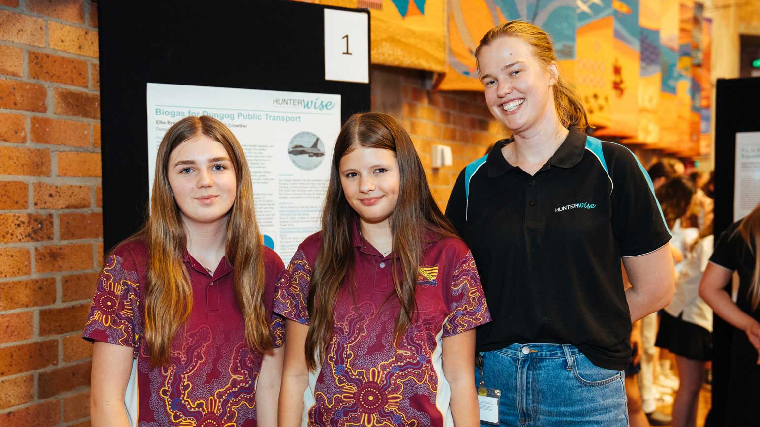 Two students from Dungog High School wearing their burgundy uniform t-shirts featuring Aboriginal artwork, standing with their HunterWISE mentor, a blonde female wearing a black t-shirt.