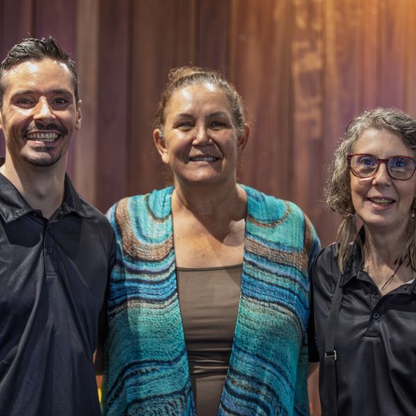 Three people are closely pictured smiling to the camera, a man and two women.