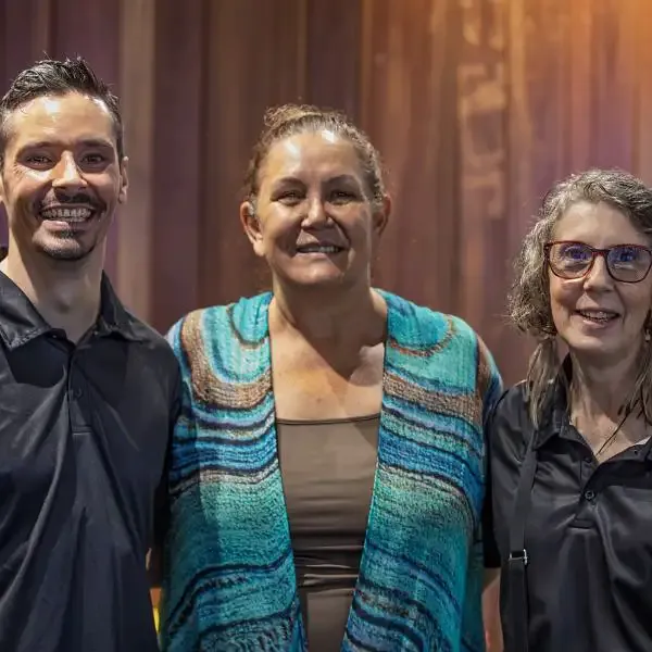 Three people are closely pictured smiling to the camera, a man and two women.