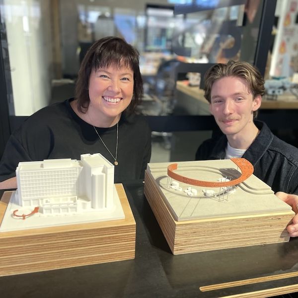 A young woman and a young man smile and pose behind a model of a building.. Student-led design creates legacy for Newcastle City Campus.