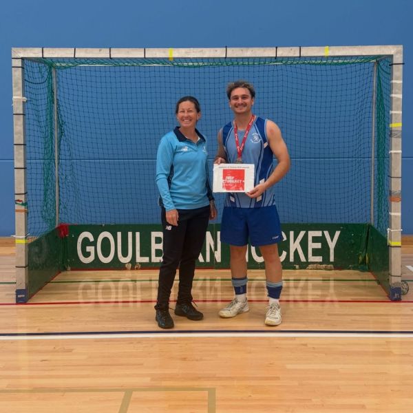 Man standing next to a woman inside a hockey net smiling