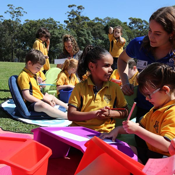 Students writing letters with the help of University Occupational Therapy student Maddie