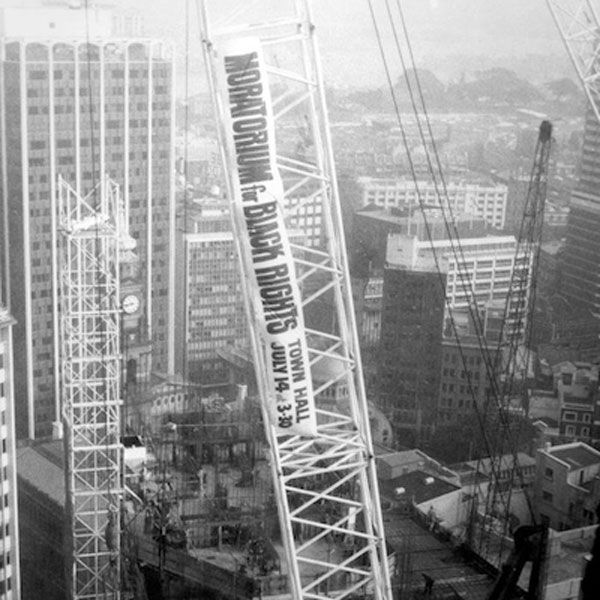 Black and white photograph of a crane, high above a cityscape, with a banner saying, 