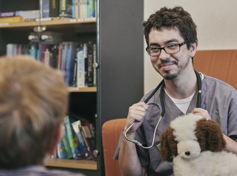 Medical student holding a teddy bear and talking to a child