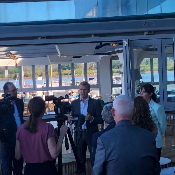 Image shows man speaking to media with water view behind him. New University campus for Gosford .