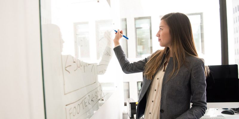 Lady writing on a whiteboard wearing a professional outfit. 