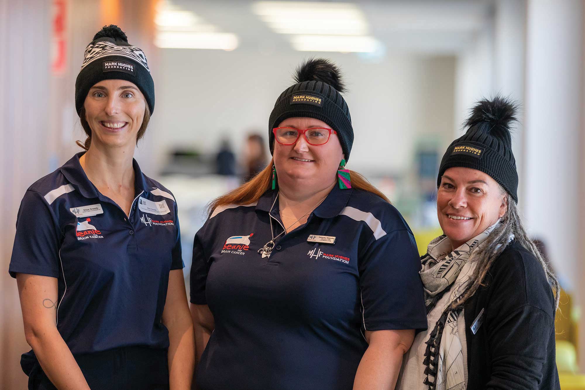 Three nurses in polo shirts and beanies smiling at the camera