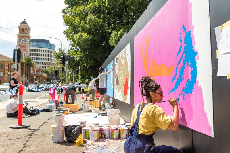 Three artists painting different murals along a wall