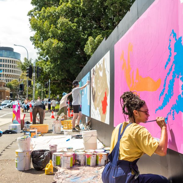 Three artists painting different murals along a wall