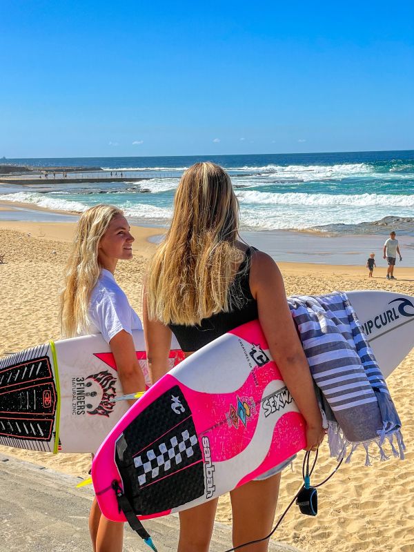 2 women holding surboards at the beach