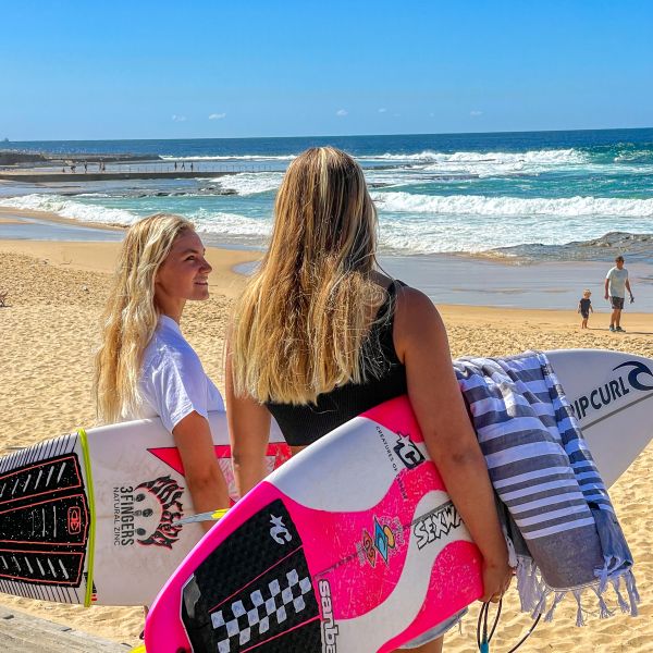 2 women holding surboards at the beach