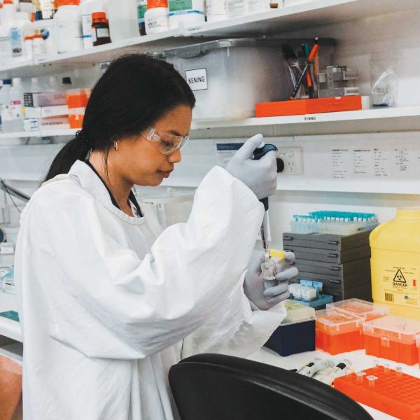 A photo of University PhD candidate student Cheenie Nieva in a white lab gown holding equipment as she is working in the lab. 