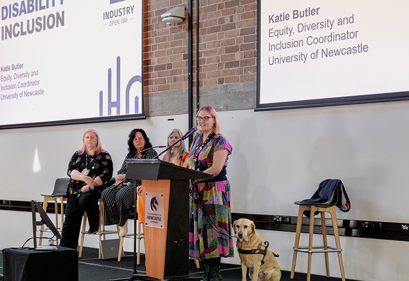 Woman with an assitance dog, standing at a podium on stage
