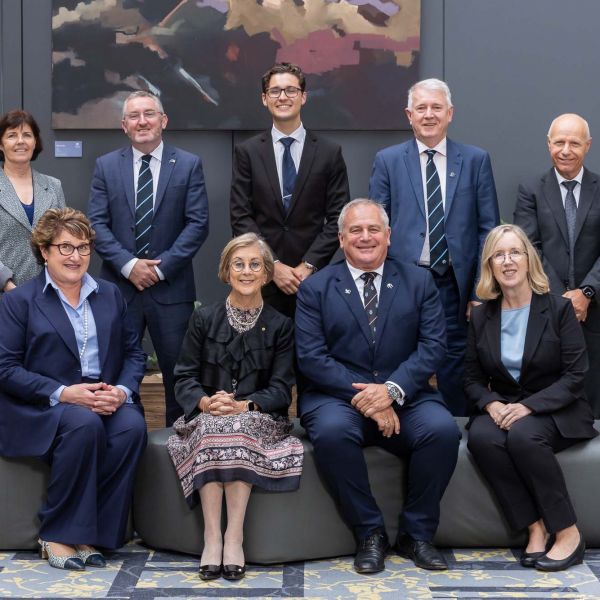 Group portrait of 2023 University Council in formal attire, smiling in an office setting with a modern art piece in the background.. University Council increases its student representation.