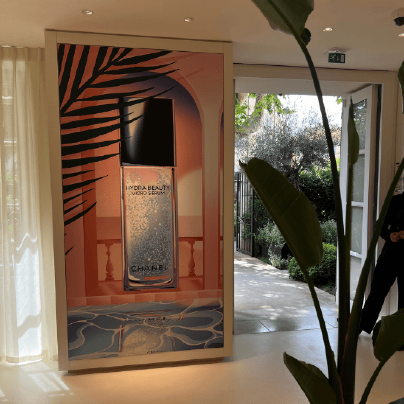 Izzy's design for Chanel set behind a glass wall, framed by indoor plants and softly lit curtains.