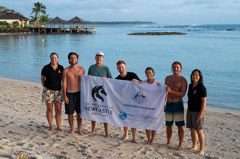 Group of people standing on a beach holding up a banner