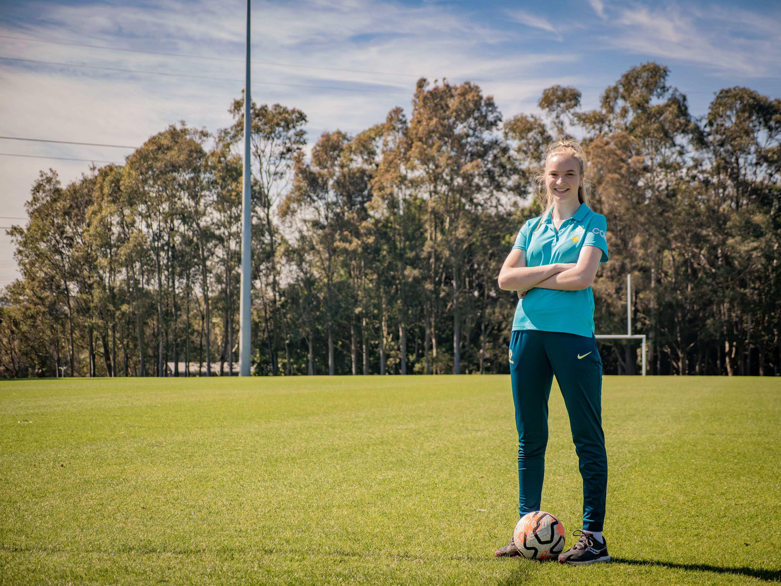 Lainee Harrison won Sports Person of the Year Lainee Harrison stands on a green football field smiling with her arms crossed, there are tall green trees in the background