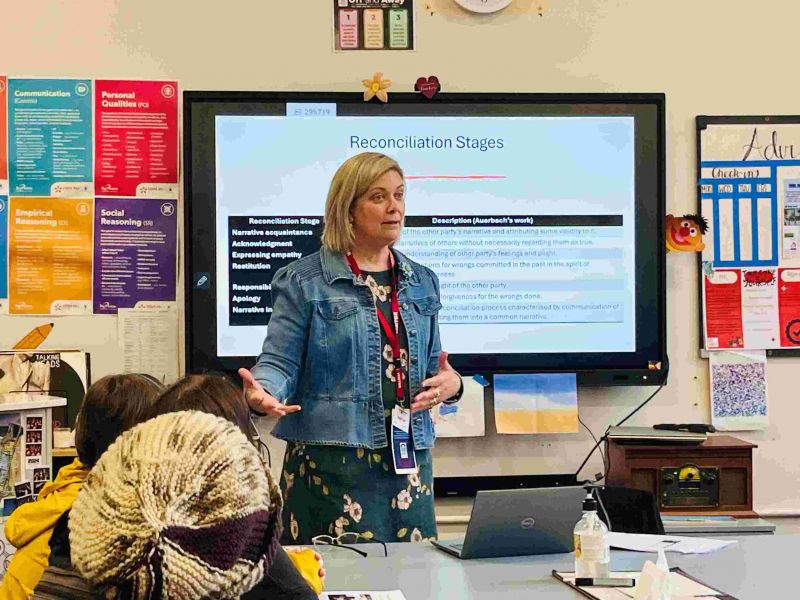 Head and shoulders shot of a middle-aged woman with short blond hair in from of a class