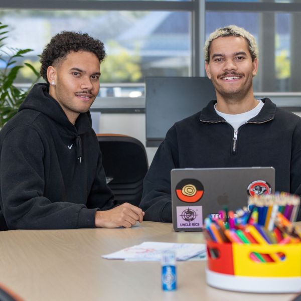 Bailey and Leigtham (twin brothers) sit side by side at a desk smiling at the camera. . Central Coast twins tackle university to support local mob.