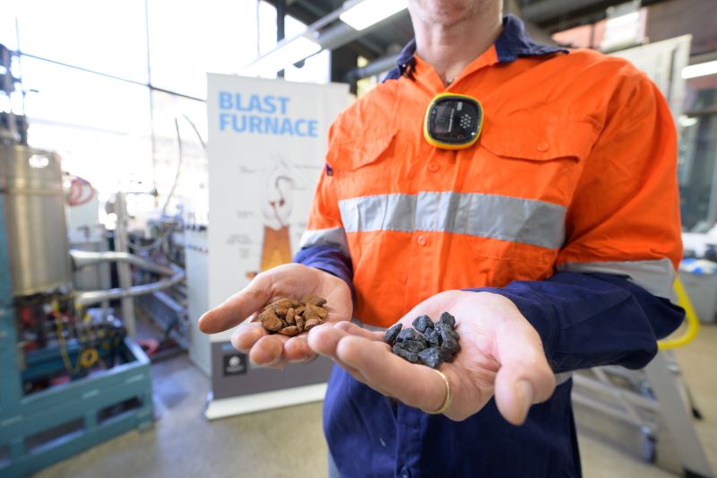 Man holding two types of pellets in his hands with Blast Furnace sign in the background
