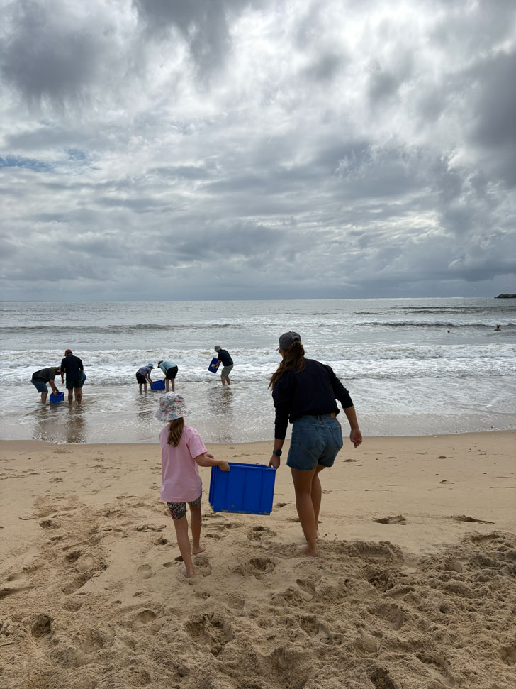 Community members carry blue tubs to the water at the beach