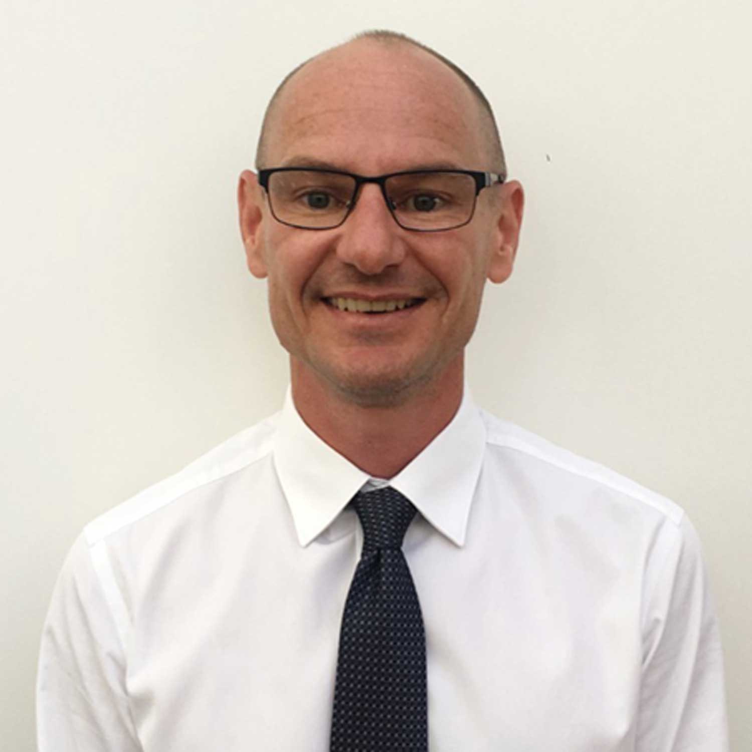 Man wearing glasses smiling at the camera, pictured against a white backdrop.
