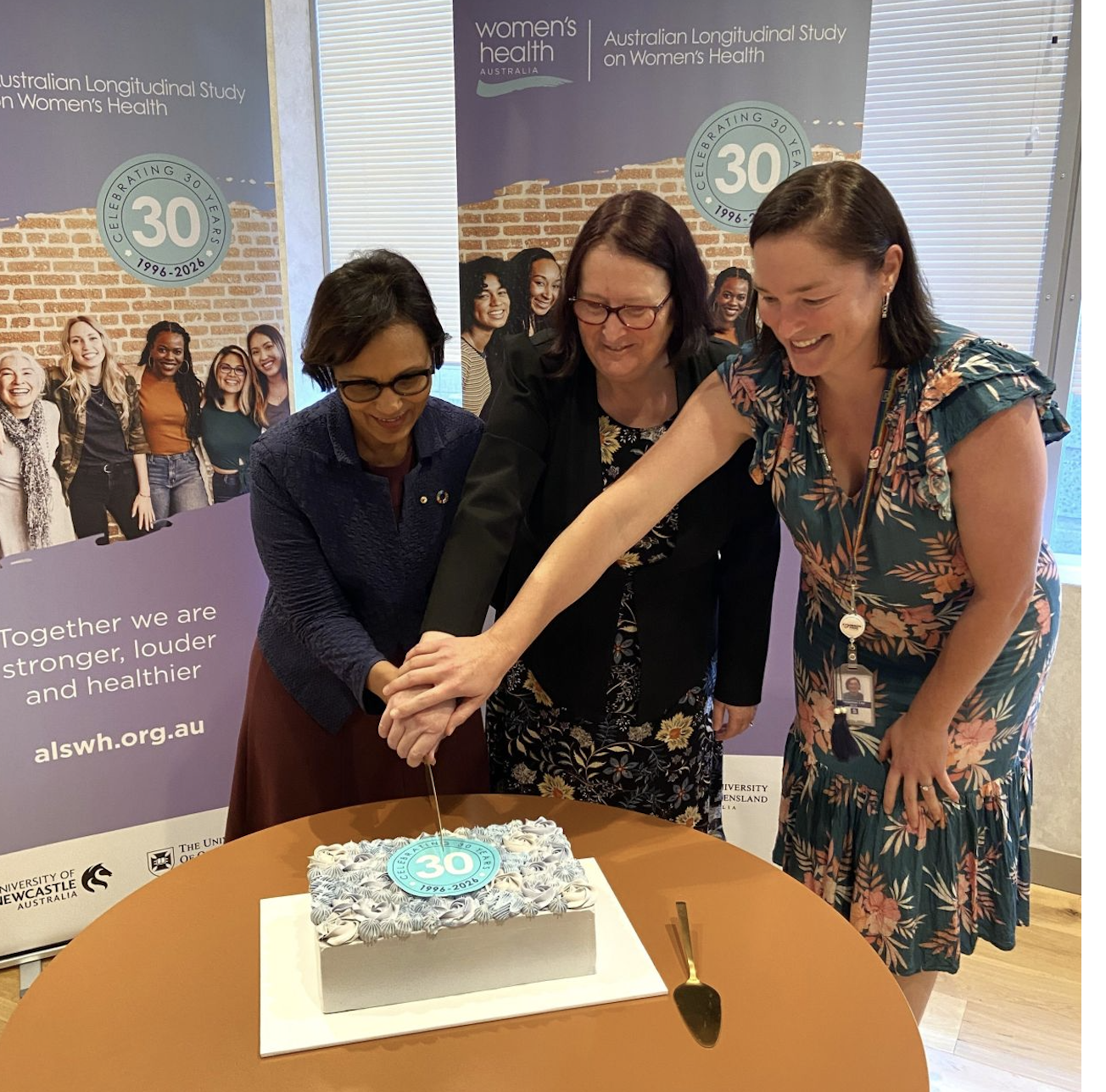 Three women cut a cake together