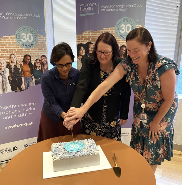 Three women cut a cake together