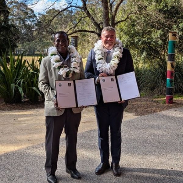 Two men standing side-by-side, holding documents and smiling for the camera