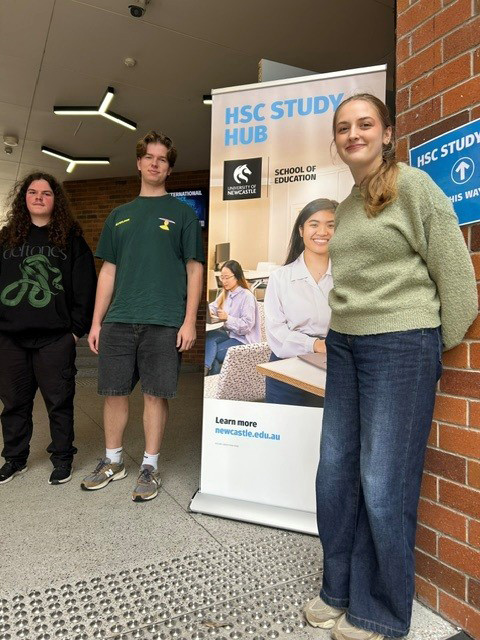 Three HSC Study Hub students pose next to a HSC Study Hub banner outside the lecture theatre