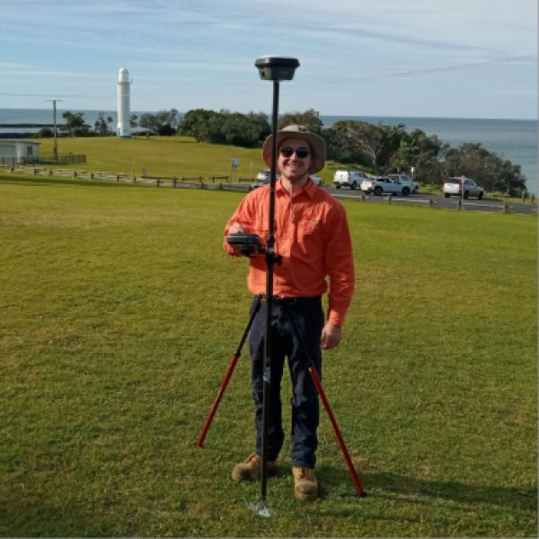 Joshua standing on hill with with surveying equipment in the background smiling at camera