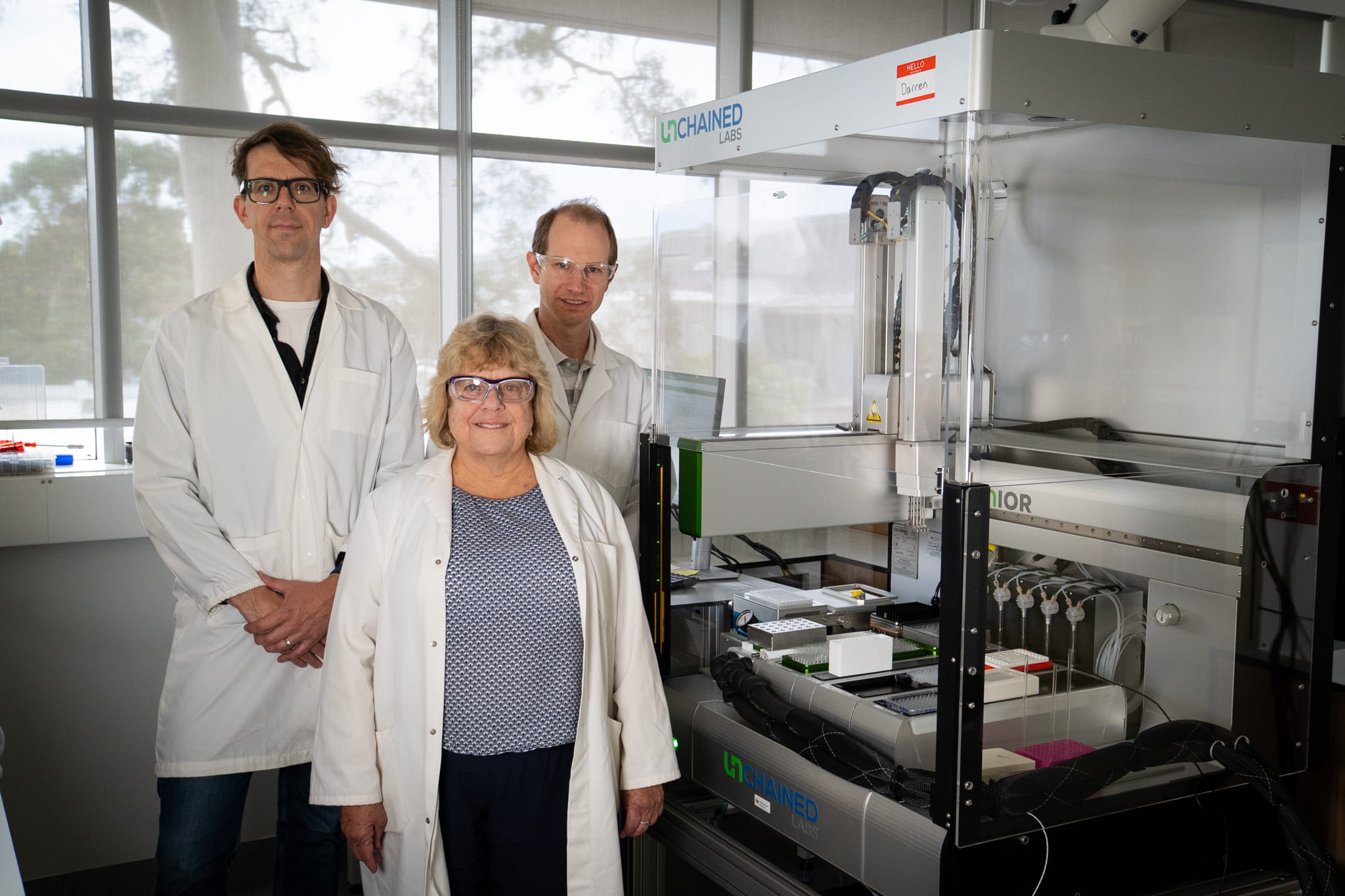 three scientists stand smiling to camera with the robot equipment in the background