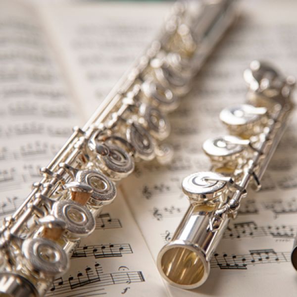 A silver flute rests on open sheet music, with the instrument’s keys and polished metal surface in sharp focus against a softly blurred musical score.