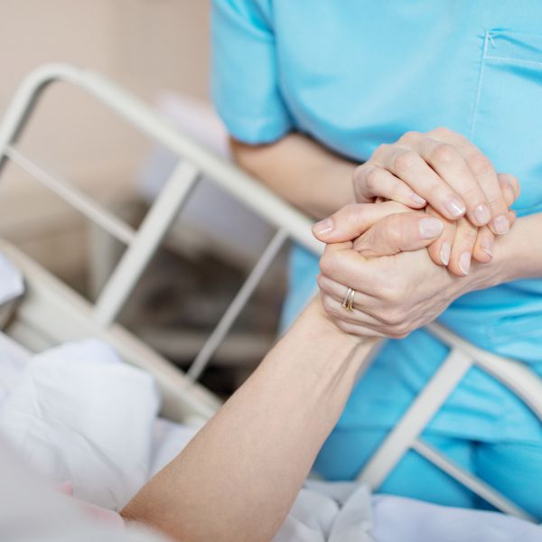 Nurse holding patient hand. Improving mental health support for cancer and palliative care patients