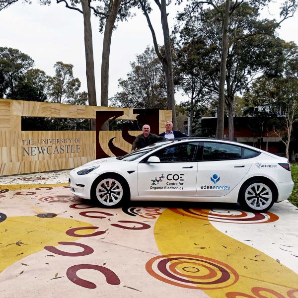 Two men behind a car if front of a University of Newcastle statue. Epic road test for printed solar 