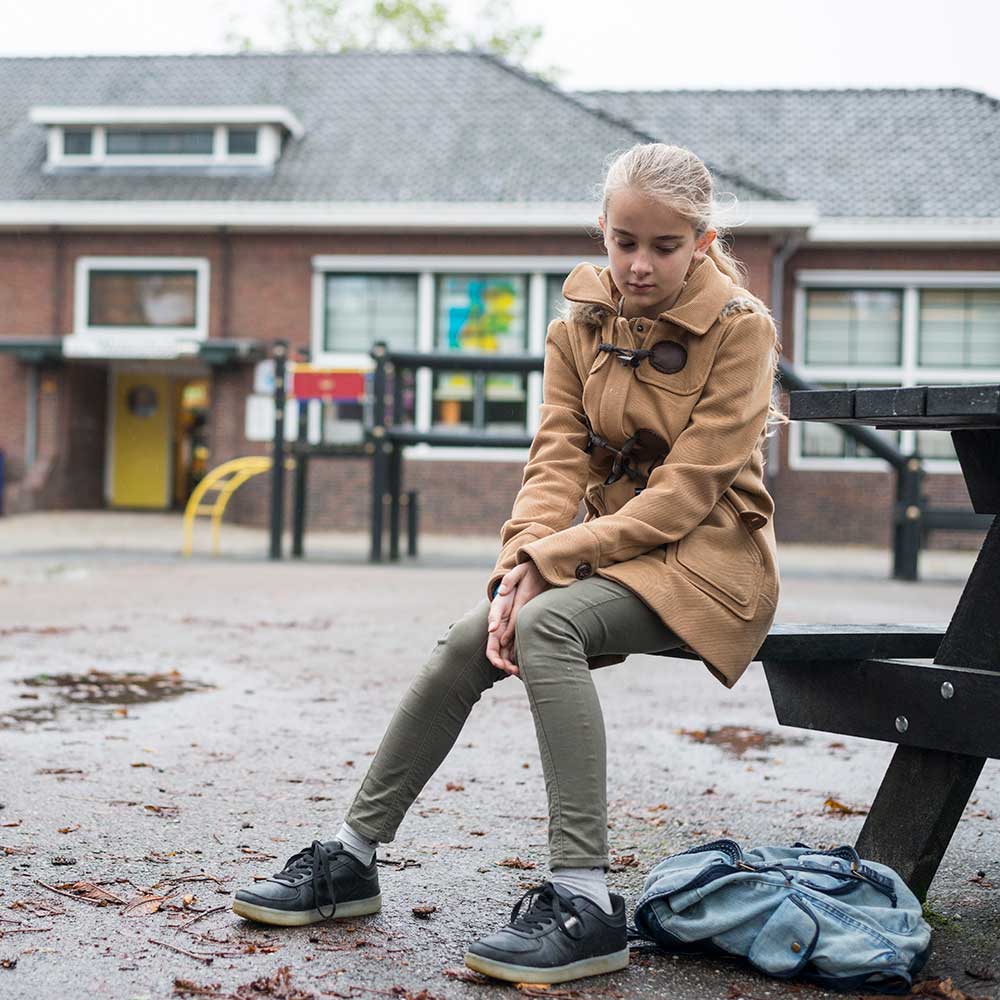 Girl sadly sitting alone in school yard. 