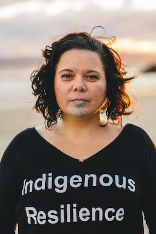 Dr Tina Ngata stands with a black t-shirt saying Indigenous resilience