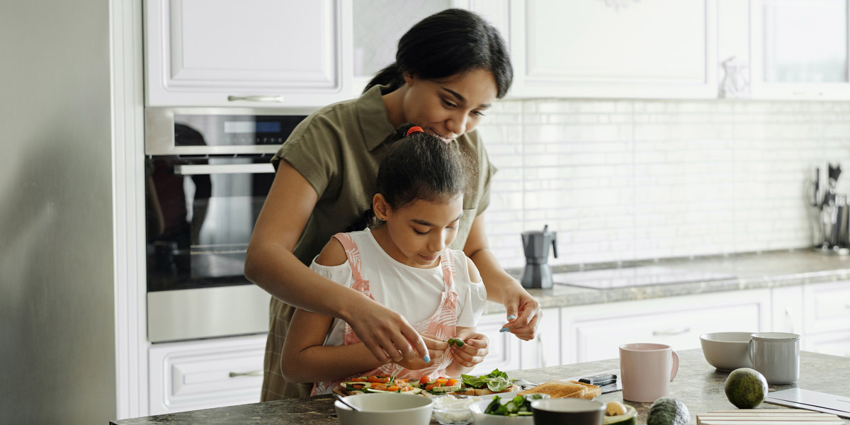 A mother helping her child to prepare a meal in the kitchen. 