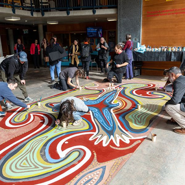Staff work to restore the birabahn eagle painting on the floor of the Wollotuka building 