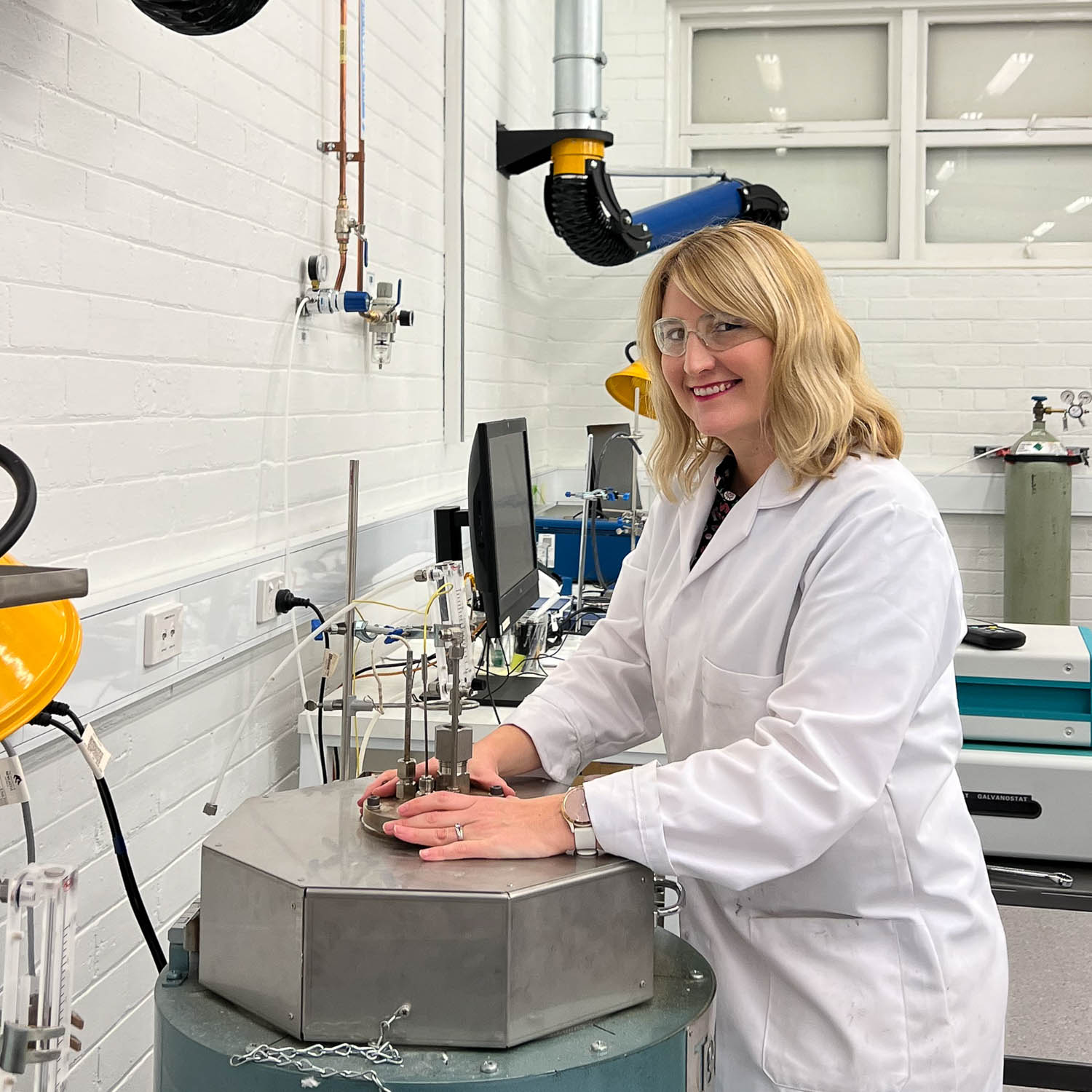researcher, Dr Jessica Allen, stands in her lab wearing a white lab jacket holding science equipment smiling at the camera^empty:{ds__assetid^as_asset:asset_name}